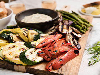 grilled vegetables arranged on cutting board surrounded by herbs with garlic mustard sauce on side
