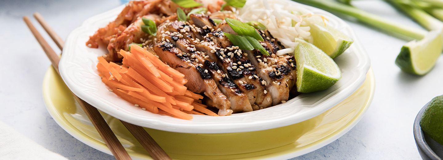 barbecued chicken garnished with carrots, sliced ginger and lime in a bowl with chopsticks resting on the side